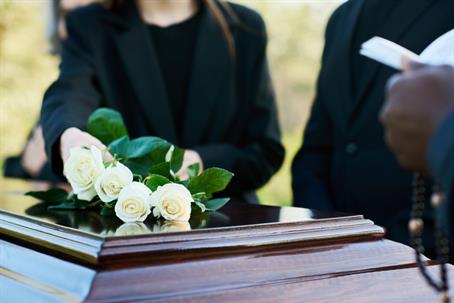 person putting roses on top of closed coffin at a funeral service