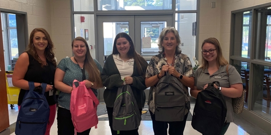Four women with backpacks, casual attire.