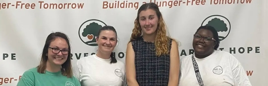 Four people are smiling in front of a banner